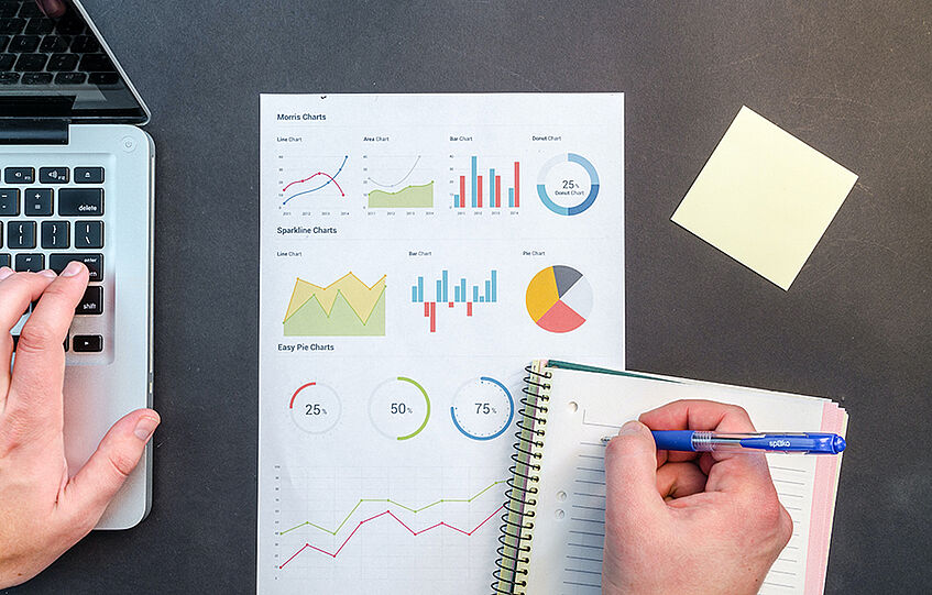 Picture shows diagrams and graphs on a piece of paper, a notebook and a laptop.