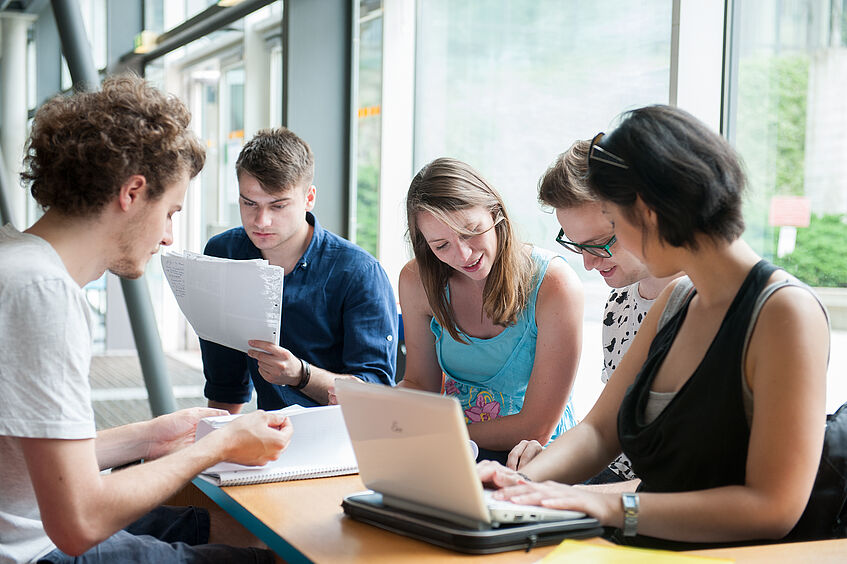 Fünf Studierende sitzen beim Lernen/Arbeiten zusammen.